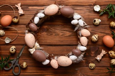 Ahşap arka planda yumurta ve tüylerle süslenmiş şık bir Paskalya çelengi. Üst görünüm