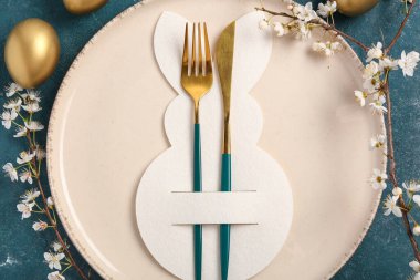 Mavi grunge arka planında Paskalya yumurtaları ve çiçek açan kiraz dalı olan masa ayarı, yakın plan.