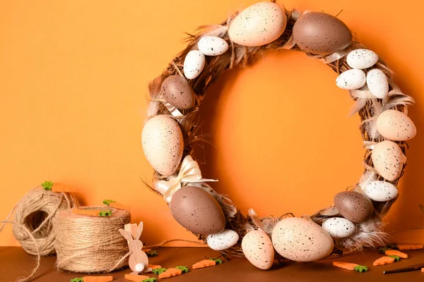 Turuncu arka planda tüy ve yumurtalarla süslenmiş sevimli geleneksel Paskalya çelengi.