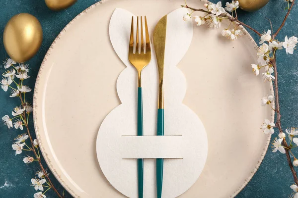 Mavi grunge arka planında Paskalya yumurtaları ve çiçek açan kiraz dalı olan masa ayarı, yakın plan.