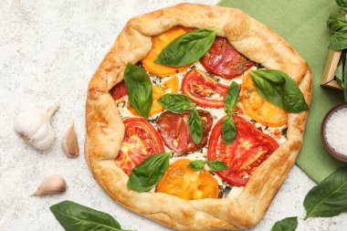 Tasty tomato galette with fresh basil and garlic on light background