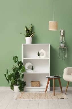 Çiçekler, kahve masası, raf ünitesi ve odanın yeşil duvarının yanında asılı duran lamba.