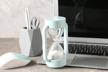 Çalışma masasında beyaz kum, kırtasiye ve dizüstü bilgisayarlı kum saati.