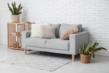 Raflama ünitesi, kanepe ve sansevieria çiçekleri odanın içindeki beyaz tuğla duvarın yanında.