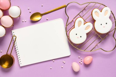 Tarifler için boş defter, eflatun arkaplanda paskalya yumurtası ve kurabiye kompozisyonu