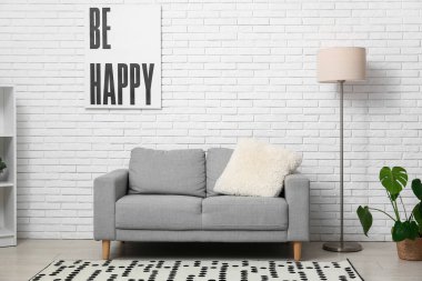 Aydınlık oturma odasında yerde lamba olan gri kanepe.