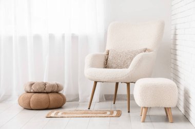 Büyük pencerenin yanında beyaz koltuklu ve puf pufları olan aydınlık oturma odasının içinde.