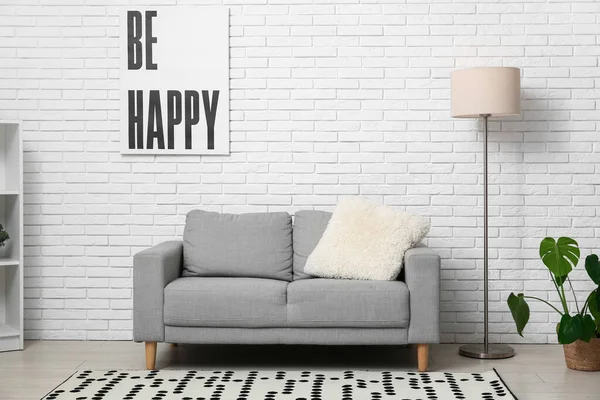 Aydınlık oturma odasında yerde lamba olan gri kanepe.