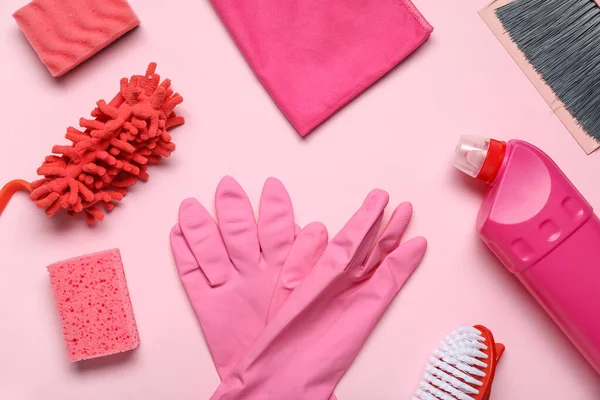 Farklı temizlik malzemeleri ve pembe arka planda bir şişe deterjan içeren kompozisyon.