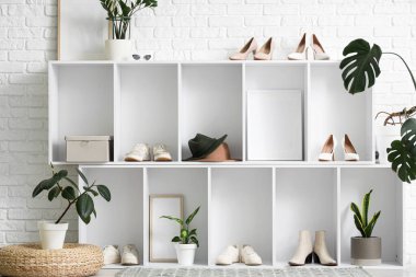 Kadın ayakkabılı raflar ve koridordaki beyaz tuğla duvarın yanındaki bitkiler.
