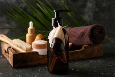 Dev Achatina salyangozları ve koyu arkaplanda spa aksesuarları olan bir şişe kozmetik ürünü.