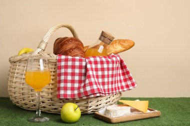 Rattan piknik sepeti, yanında meyve suyu, baget ve kruvasan ile bej duvarın yanındaki yeşil masada.