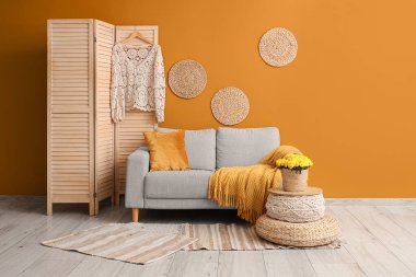 Oturma odasının içinde rahat bir kanepe, puf ve sonbahar çiçekleri.