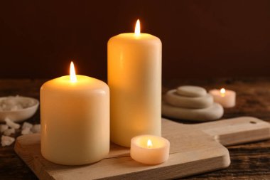 Burning candles with sea salt and spa stones on wooden table against brown background