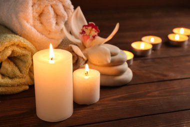 Mumları kaplıca taşlarıyla yakmak, havlular ve orkide çiçekleri ahşap masada, yakın plan.