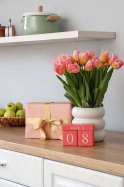 Uluslararası Kadınlar Günü tarihli takvim, laleler ve hediye kutusu mutfakta tezgahta.