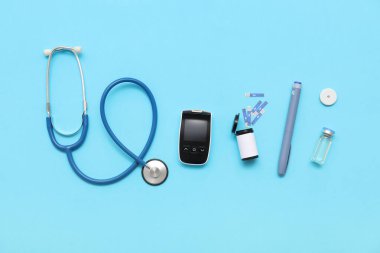 Mavi arka planda glukometre, glikoz sensörü, insülin ve steteskop. Diyabet kavramı