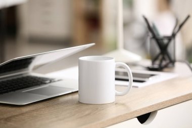 Ofisteki dizüstü bilgisayarın yanındaki masada seramik bardak.