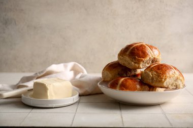 Paskalya haçı çörekleri, tereyağı ve bıçaklı tabaklar beyaz fayans masasında grunge arka planında