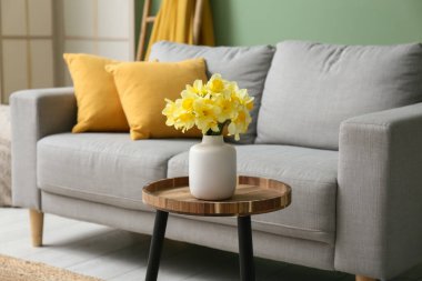 Oturma odasındaki yeşil duvara karşı kahve masası ve narsis çiçekleri olan rahat kanepe.