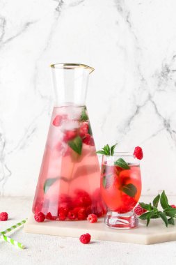 Beyaz arka planda naneli bir şişe ve bir bardak taze ahududu limonatası.