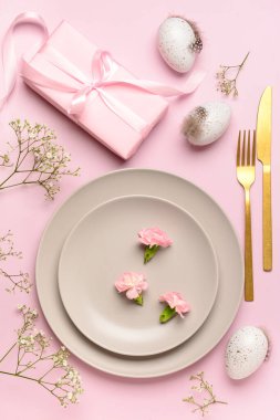Şirin Paskalya sofrası, pembe arka planda hediyeler, çiçekler ve yumurtalar.