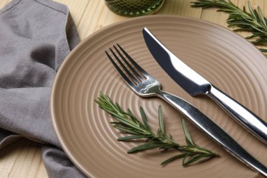 Ahşap arka planda peçete, çatal bıçak ve biberiye ile şık masa ayarları