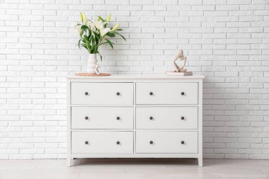 Beyaz tuğla duvarın yanındaki çekmecede çiçekli vazo.