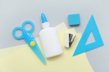 Bir şişe tutkal, makas ve gri arka planda kağıtlar. Üst görünüm