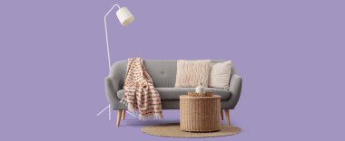 Yastıklı gri kanepe, hasır sepet ve leylak arka planda yer lambası.