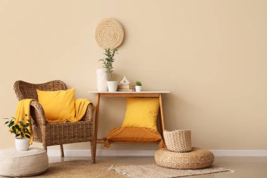 Yastıklı konsol masası, ev bitkileri ve bej duvarın yanındaki hasır koltuk.