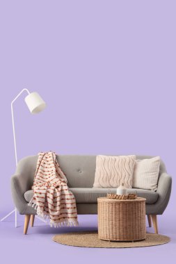 Yastıklı gri kanepe, hasır sepet ve mor arka planda yer lambası.