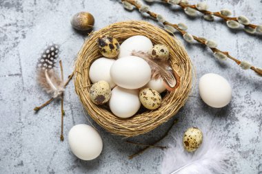 Paskalya yumurtaları, tüyleri ve gri grunge arka planında söğüt dalları olan yuva.