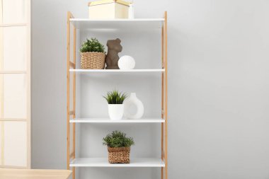 Raflarda bitkiler, hasır sepetler ve ışık duvarının yanında dekor var.