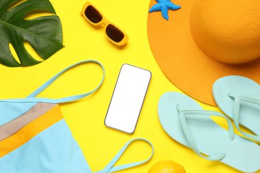 Modern cep telefonlu kompozisyon, plaj aksesuarları, mayo ve sarı arka planda palmiye yaprağı.