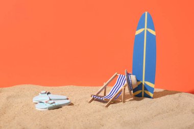 Kumlu yaz kompozisyonu, dekoratif sörf tahtası, parmak arası terlikler, kırmızı arka planda iskemle ve şapka, yakın plan.