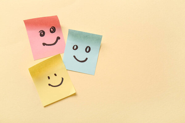 Липкие бумаги с нарисованными счастливыми лицами на бежевом фоне