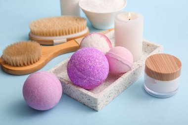 Tepsi, banyo bombaları, yanan mum ve mavi arkaplanda kozmetik ürün kavanozu, yakın plan.