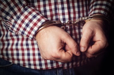 Criminal hands locked in handcuffs on dark background clipart
