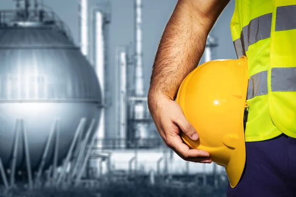 Hand or arm of engineer hold yellow plastic helmet in front of oil refinery industry — Stock Photo, Image