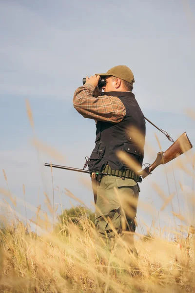 Muž lovec s brokovnicí při pohledu dalekohledem v lese — Stock fotografie