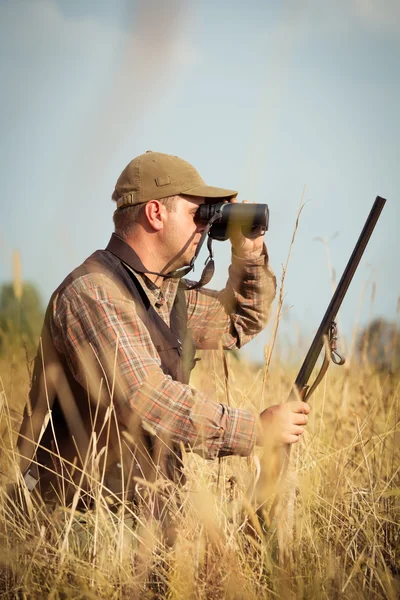 Jäger mit Schrotflinte blickt durch Fernglas in Wald — Stockfoto