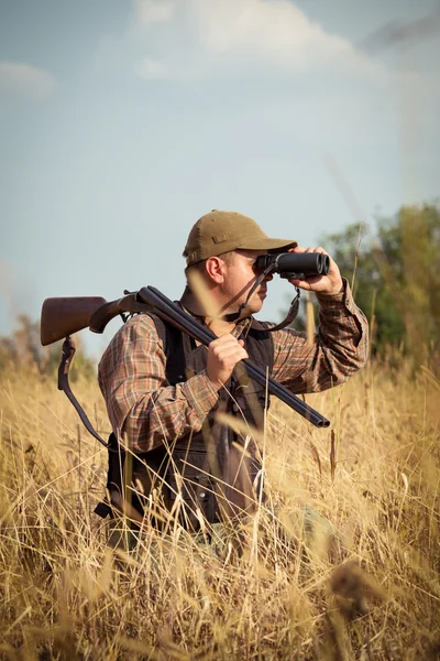 Uomo cacciatore con fucile guardando attraverso binocoli nella foresta — Foto Stock