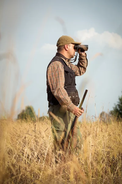 Man jägare med hagelgevär tittar genom kikaren i skogen — Stockfoto