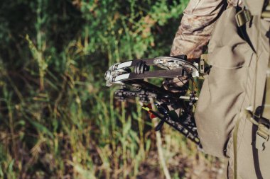 Avcı kamuflaj elbisesi giymiş, elinde modern bir yay tutuyor..