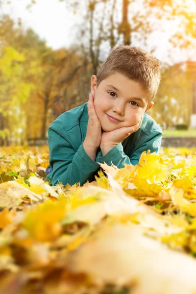 Küçük çocuk sonbahar parkında sarı yaprakların üzerinde yatıyor. — Stok fotoğraf
