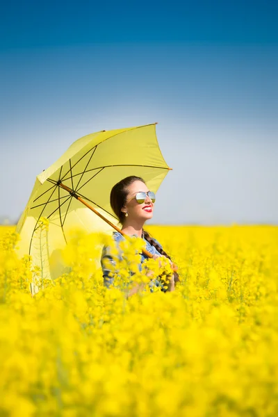 Jonge vrouw met een paraplu in canola veld — Stockfoto