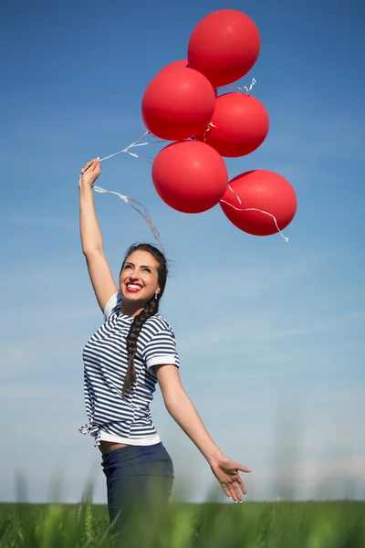 Jovem feliz com um balão vermelho em um prado verde — Fotografia de Stock
