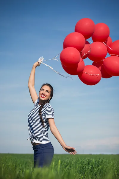 Yeşil çayır üzerinde kırmızı bir balon ile mutlu bir genç kadın — Stok fotoğraf