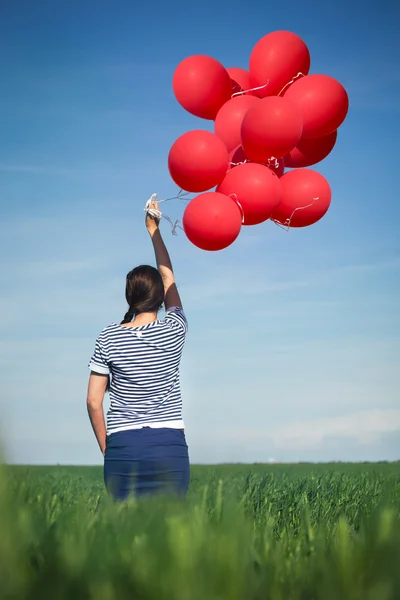 Wanita muda yang bahagia dengan balon merah di padang rumput hijau — Stok Foto